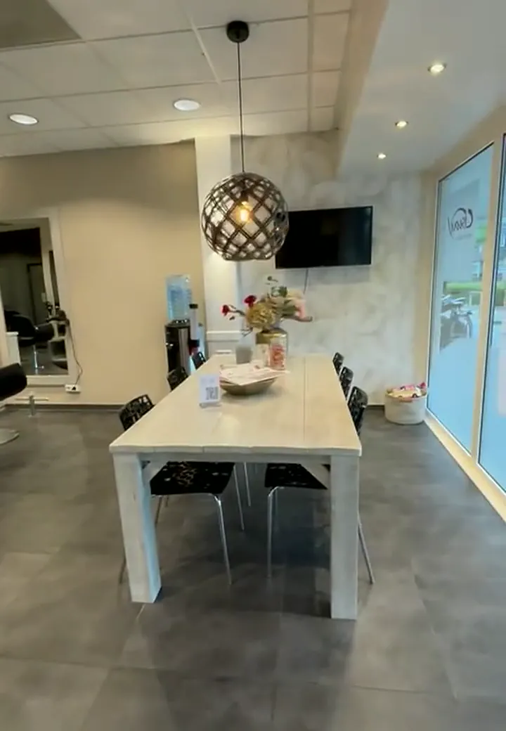 De lange tafel bij het raam, achter in de salon
