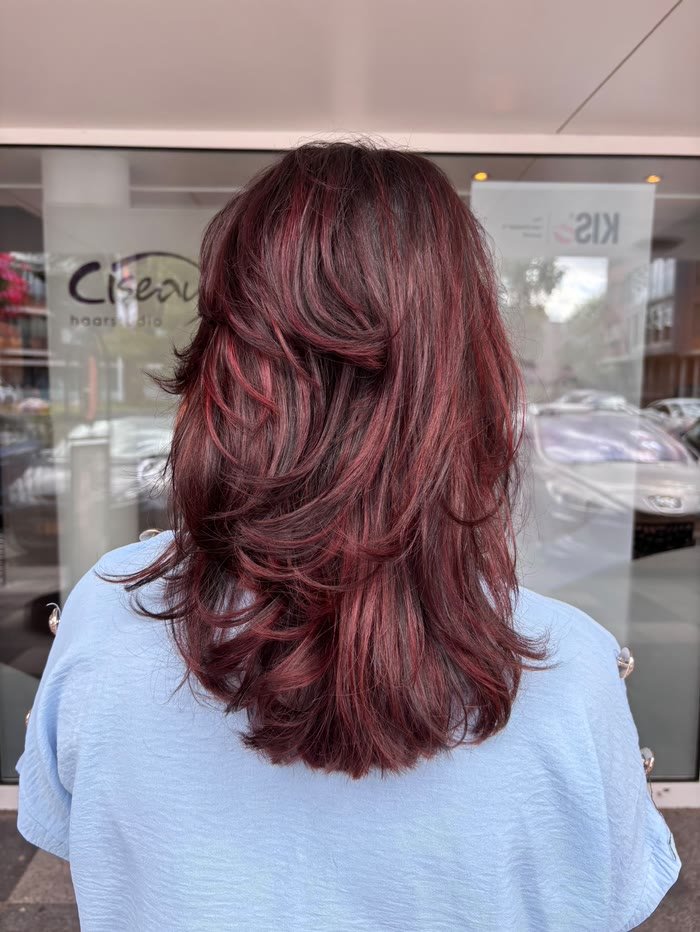 Bordeauxrode laagjes met krullende punten, voor het raam van de salon